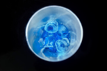 Blue cold syrup with ice in a tool for mixing and making alcoholic cocktails shaker on a black background, close-up