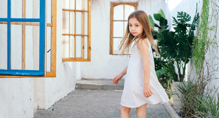 Fototapeta premium Beautiful girl with long hair in a white sundress in a light Balinese courtyard Greece Santorini vacation