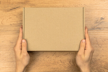 Obraz premium Delivery man with cardboard box mockup, top view. Wooden table background. Suitable for food, cosmetic or medical packaging. Shipping and delivery concept