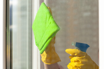 hand in a yellow rubber glove wipes the window close-up