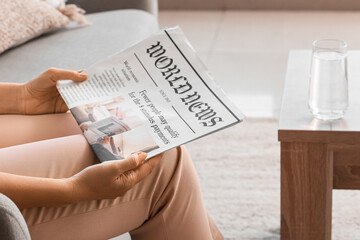 Naklejka premium Mature woman reading newspaper on sofa at home, closeup