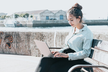 Young african american Businesswoman sitting on a bench at the shore outdoors working on laptop...