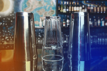 2 shakers of bar instruments for mixing and preparing alcoholic cocktails and drinks with a glass on the bar counter