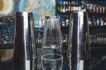 2 shakers of bar instruments for mixing and preparing alcoholic cocktails and drinks with a glass on the bar counter