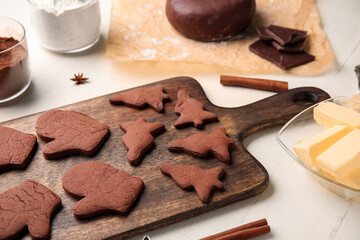 Board with tasty chocolate Christmas cookies and ingredients on white wooden background, closeup