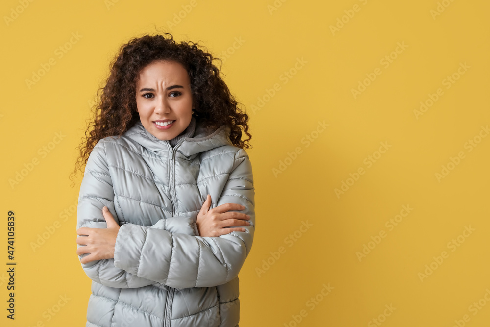 Wall mural Freezing African-American woman in winter clothes on color background