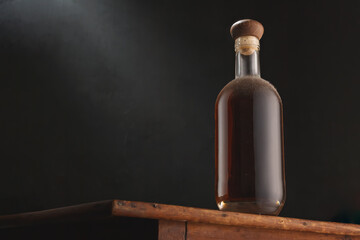 Old vintage bottle of whiskey or brandy, rum or cognac with dust on rustic table, black background. Alcohol drink, no label. Copy space, close up