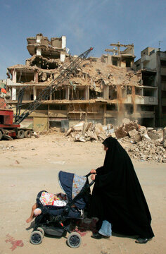 A woman pushes her baby in a stroller past a building destroyed in last summer's war between Israel and Hezbollah guerrillas in Beirut's suburbs