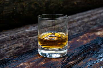 Glass of strong scotch single malt whisky on old log soaked in creosote
