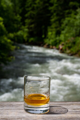 Glass of strong scotch single malt whisky with fast flowing mountain river on background