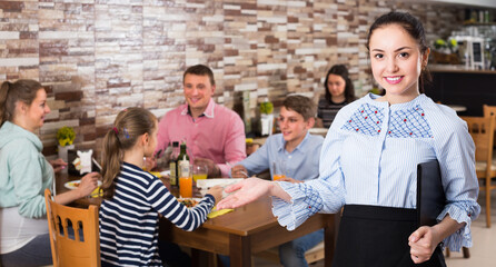 Charming young waitress warmly welcoming guests to comfortable family cafe