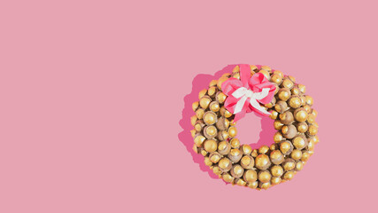 Fototapeta na wymiar Gold Christmas wreath with pink ribbon bow isolated on patel pink backgroud. Minimal Christmas flat lay concept.