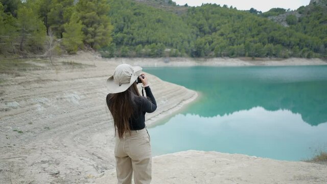 Young woman walks and takes pictures of still lake and forest in Spain