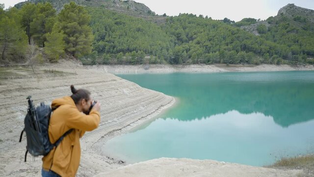 Side view of man with backpack photographing lake by Guadalest, Spain
