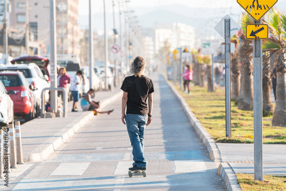 Wall mural latin mature or senior man skateboard on bikeway in La Serena at sunset