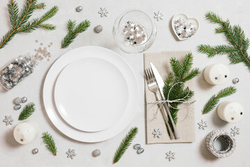 Christmas table setting with silver decorations and fir branches on gray background. Empty white plate for design. Top view, flat lay.