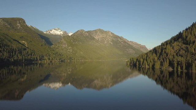 Smooth mountain lake with snowy peak behind pine forest 