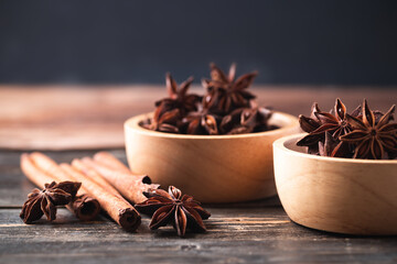 Star anise in bowl and cinnamon stick on wooden background
