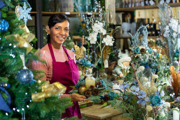 Latino american saleswoman in apron selling christmas decorations at shop for