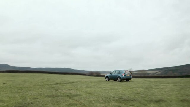 Cinematic follow drone shot of farmer driving 4x4 around an empty field