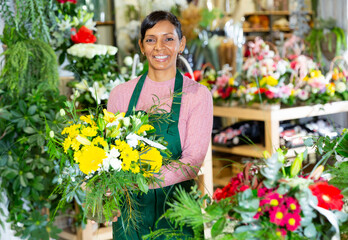 Fototapeta na wymiar Positive mexican female florist in apron holding composition from natural flowers at flower shop