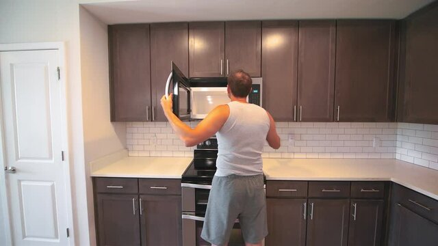 Man checking inspecting modern electric microwave oven opening at kitchen room at modern apartment by clean brown cabinets