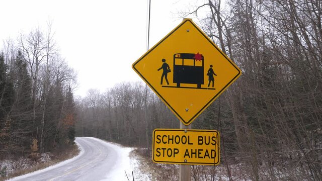 School Bus Stop Ahead sign on rural road. Snow falling. Winter in Haliburton County, Ontario, Canada.