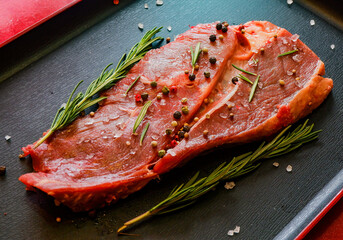 beef steak sprinkled with spices with rosemary on a black background