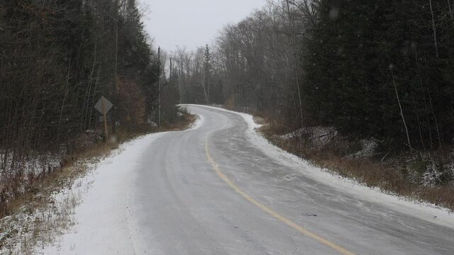 Curvy rural winter road. Slow motion shot with light snow falling. Haliburton, Ontario, Canada. Handheld shot with stabilized camera.
