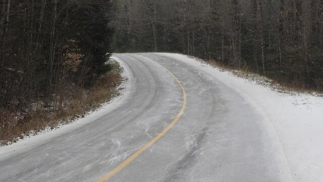 Corner on rural winter road. Slow motion shot with light snow falling. Haliburton, Ontario, Canada. Handheld shot with stabilized camera.
