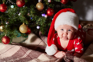 Caucasian baby shows his tongue and crawls under the Christmas tree at home. lifestyle. copy space