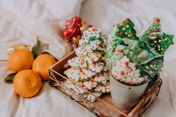 Christmas sweets, gingerbread painted with icing, lollipops and meringues in the shape of Christmas trees and tangerines on a beautiful tray. homemade cakes. delicious food for the winter holidays
