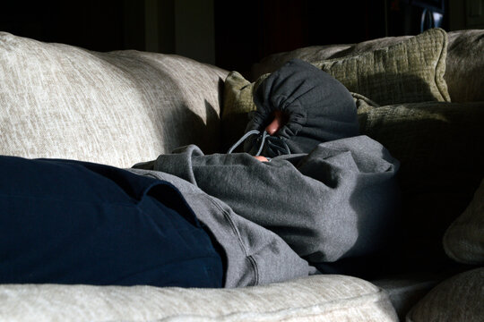 Introverted or depressed man with hood pulled shut lying on a couch