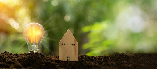 Bright light bulb and simulated wooden house on the mound. Concept for realty, economy, finance, Daytime, nature, clear air. Light of shine in the morning. Copy space, Blurred, bokeh, green background