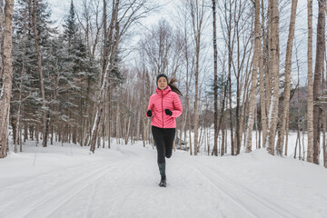 Winter Woman Running in Snow. Runner working out outside on winter day in forest. Fit healthy lifestyle picture of beautiful young sports model. Multiracial Asian Caucasian Girl