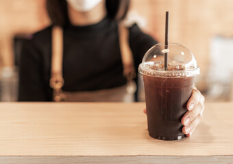 Barista in apron and face mask standing behind counter bar ready to give Coffee Service at the modern coffee shop, Modern cafe business, Social distancing concept. Holiday concept with coffee