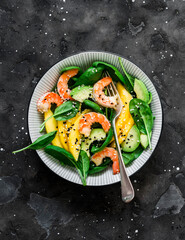 Fresh  salad with shrimp, mango, spinach and avocado on a dark background, top view