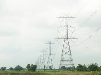 Poles and high voltage transmission lines on sky and clouds background