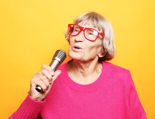 happy old woman wearing pink sweater and eyeglasses holding a microphone and singing