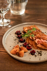 tender meat with fruits, cherries and herbs on a gray ceramic plate on a wooden table with a glass of wine in a restaurant in the evening