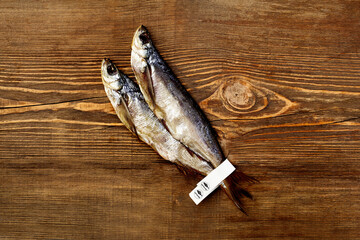 Two salted air-dried sabrefish with paper labels on tails on wooden background