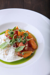 Straciatella with persimmon and tomatoes.Food on a white plate. Restaurant menu concept. Close-up.