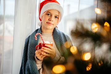 Cosy Christmas at home festive background with a girl in Santa hat and a cup of hot chocolate