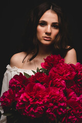 portrait of a young, beautiful and sensual woman with a lush bouquet of red peonies in her hands