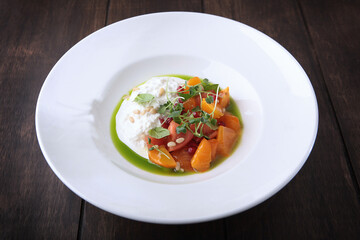 Straciatella with persimmon and tomatoes. Food on a white plate. Restaurant menu concept. Copy space. Flat lay.