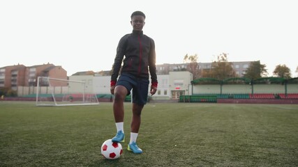 Young african american girl standing on a soccer field against the background of a gate and putting her foot on a soccer ball
