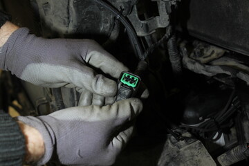 Close-up of the hands of an auto mechanic engaged in car maintenance. Car wiring with adapters and connectors turned off. A mechanic wearing gloves disconnected the connector in the car.