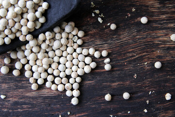 spice white pepper in a black spoon on a wooden background.