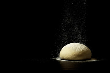 sprinkle with flour fresh homemade dough on a black background.