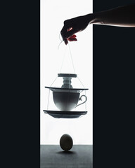 Danger of falling, stack of dishes and cups hanging over an egg, fragility concept